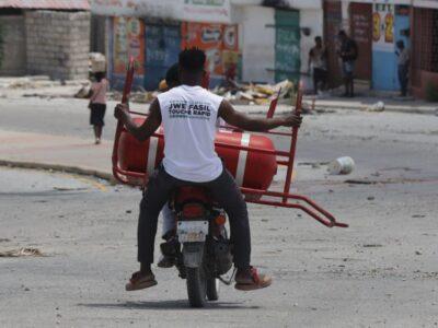 Un homme transporte une bouteille de gaz parmi les objets récupérés chez lui après le passage des gangs à Solino, le XY août 2025. Photo : Jean Feguens Regala / AyiboPost
